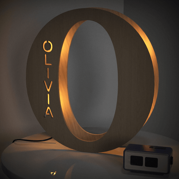 Illuminated wooden letter "O" night light with the name "Olivia" etched on the side, providing warm ambient lighting.