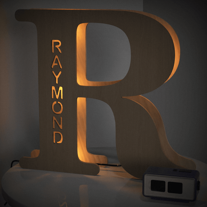 Large wooden letter R with the name Raymond illuminated by warm light, placed on a table, part of the Enchanted Woodland Alphabet Lamp collection.